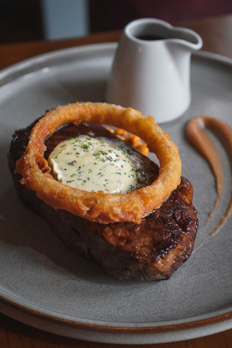 Ribeye steak topped with an onion ring and garlic butter, with peppercorn sauce